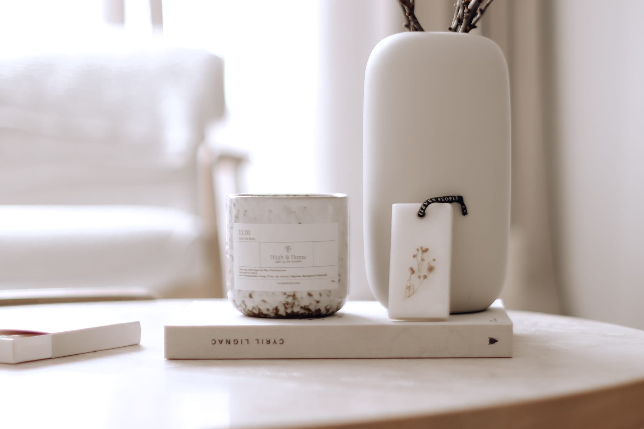 Ceramic items including a vase, candle, and book on a surface with a blurred background